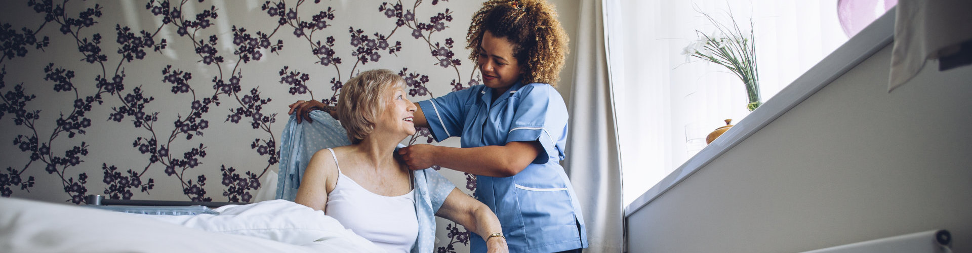 Home Caregiver helping a senior woman get dressed in her bedroom