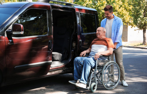 Young men helping patient in wheelchair to get into van outdoors